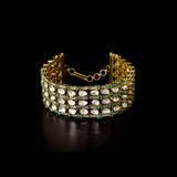 Versatile gold choker cum bracelet adorned with shimmering round diamonds, uncut diamond polki, and vibrant oval emerald accents, crafted in layered elegance to create a bold, luxurious statement for contemporary and traditional looks. (KMBR0150)