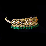 A fusion Navratan choker featuring polki diamonds in gold, highlighted with a central ruby, multicolored gemstones, intricate pearl detailing, and cascading emerald drops—paired with statement earrings for a rich, regal presence. (KMNE3719)