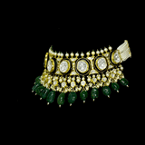 A majestic choker showcasing large polki diamonds set in striking green-enamelled gold, layered with intricate detailing, finished with cascading emerald drops and pearl fringes—opulent, bold, and exquisitely regal. (KMNE3724)