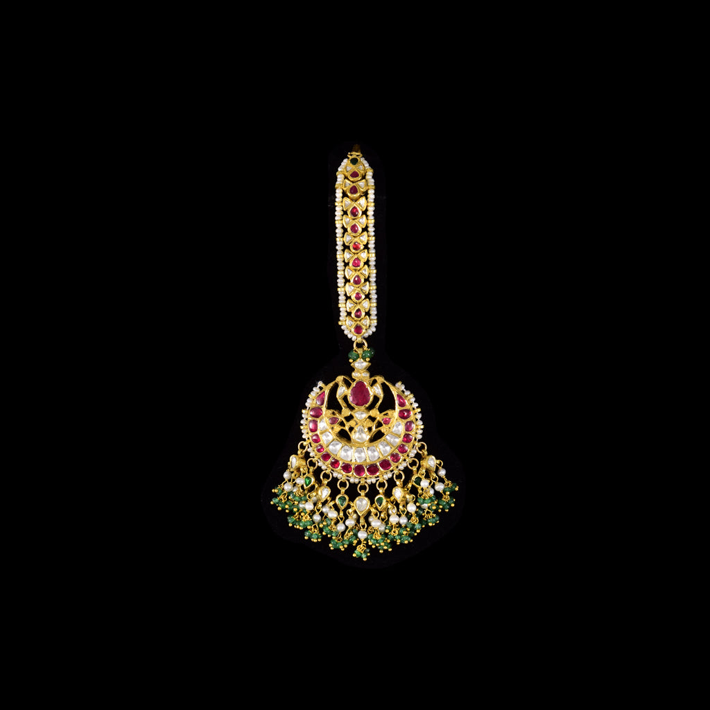 Radiate royal charm with this chand-style maangtika, featuring uncut diamond Polki and rubies, beautifully accented with emerald beads and pearls for a timeless, traditional look.(KMTK0242)