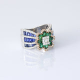 Featuring a diamond cluster center, encircled by vivid emeralds and accented with channel-set sapphires, this ring is designed to make a powerful statement. (PGDR0523)