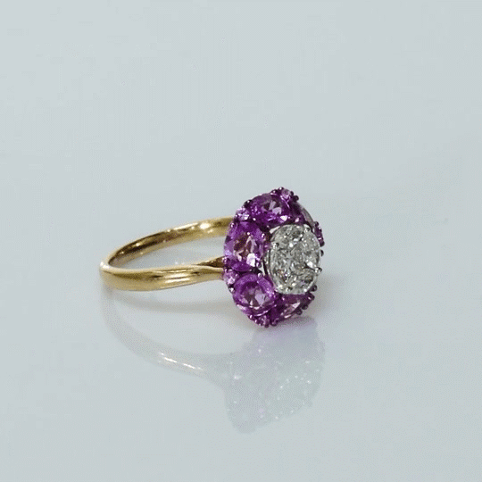 A radiant round diamond embraced by a halo of vivid pink sapphires—where timeless brilliance meets feminine charm. (PGDR0524)